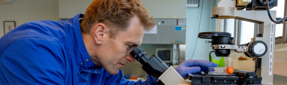 scientist in lab coat looking into a microscope