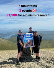Three friends on top of a mountain holding a poster 