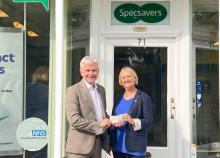 Two people smiling holding cheque under sign that says 'Specsavers'
