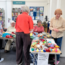 Ladies around table with lots of knitted creations displayed 