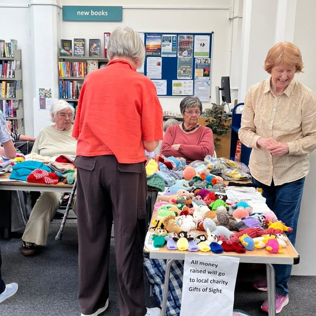 Ladies around table with lots of knitted creations displayed 